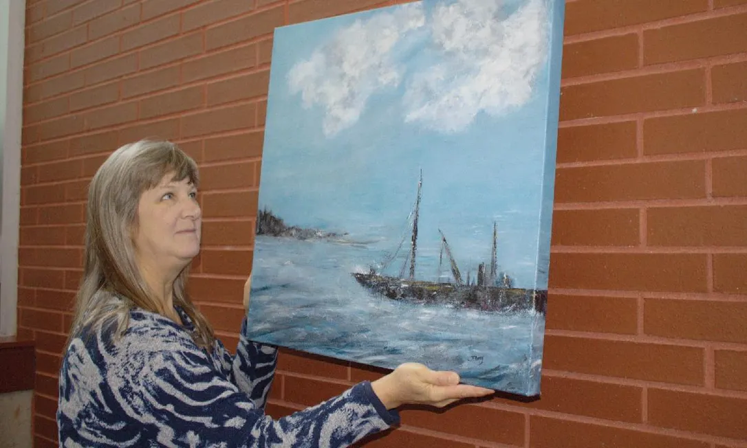 Artist Tina Clancy of Milton hangs one of her works, Inlet, at a space outside the Welland Public Library at Welland Civic Square. The popular art displays are making a return after a two-year hiatus due to the COVID-19 pandemic.